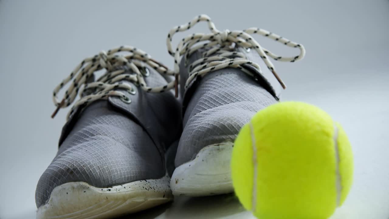 zapatos deportivos y pelota de tenis sobre fondo blanco 4k