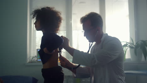 pediatrician examining teen girl lungs using stethoscope in health clinic.