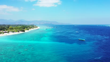 Flying-over-blue-azure-sea-full-of-boats-anchoring-near-shore-of-tropical-island-with-white-beach-and-lush-vegetation-in-Bali