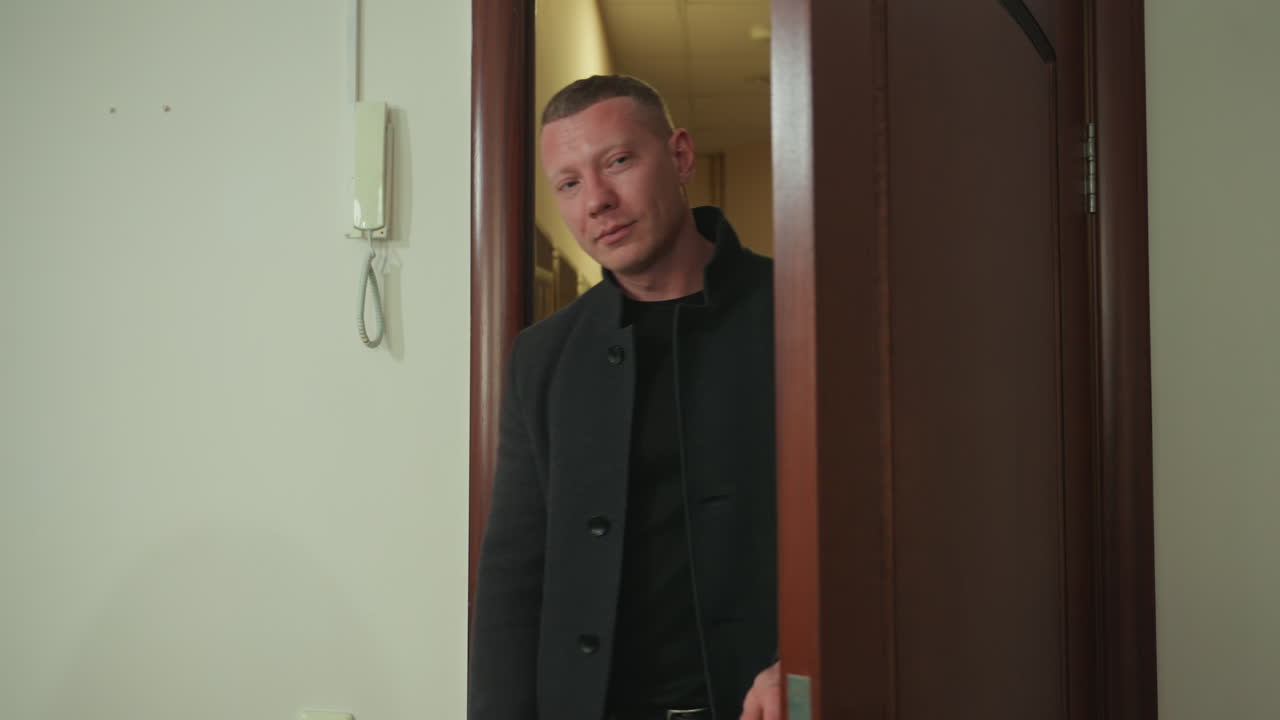 Uomo entra nella porta del corridoio della clinica, accolto da una receptionist asiatica, cappotto casual e sorriso amichevole creano un tono rilassato, dettaglio di porta in legno e interfono, rapido controllo dell'appuntamento su tablet, breve.