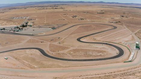 los autos corren alrededor de una pista de carreras ubicada en el desierto de mojave - vista aérea a cámara lenta