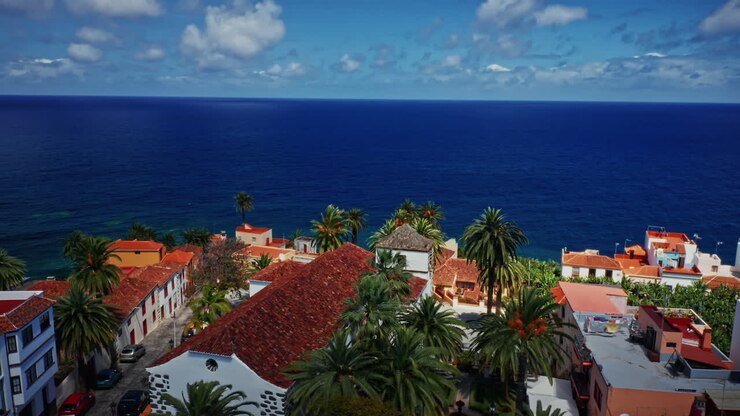 Aerial drone shot over a beautiful local town located at the coastline in La Palma, Canary Islands, Spain.
View of the deep blue sea and the palm trees.