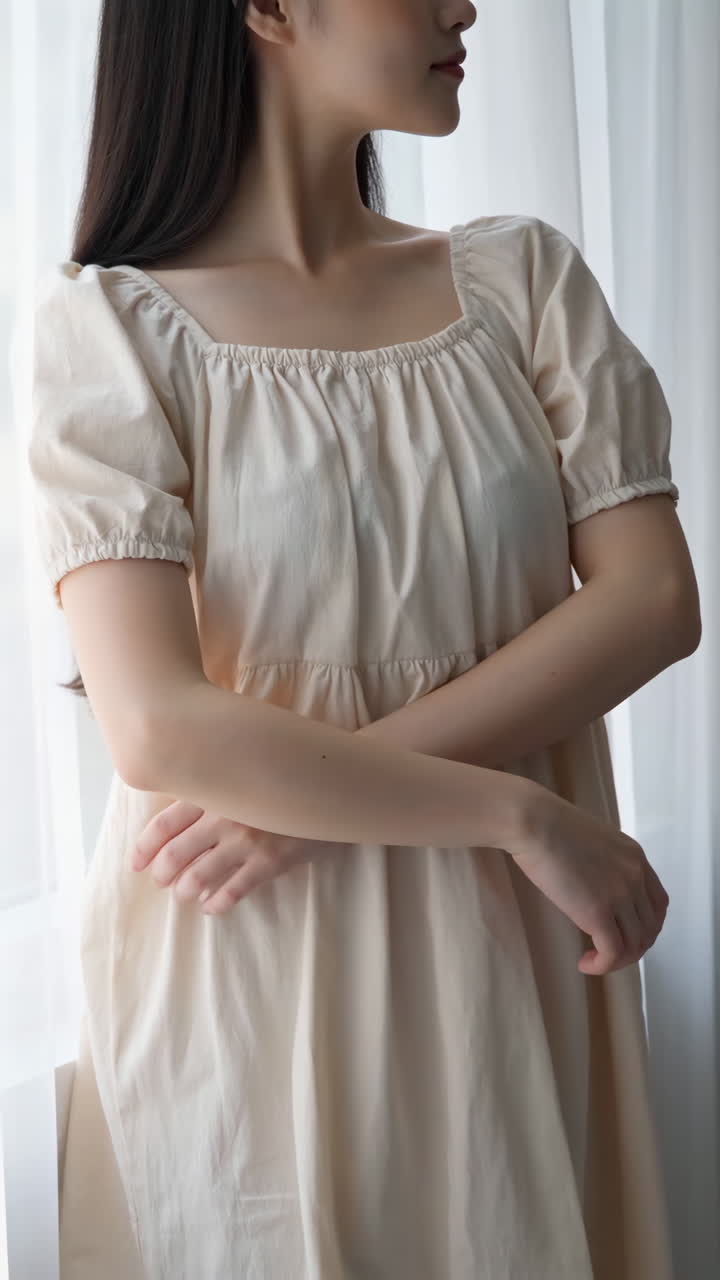 Woman in a Light Dress Standing by a Window