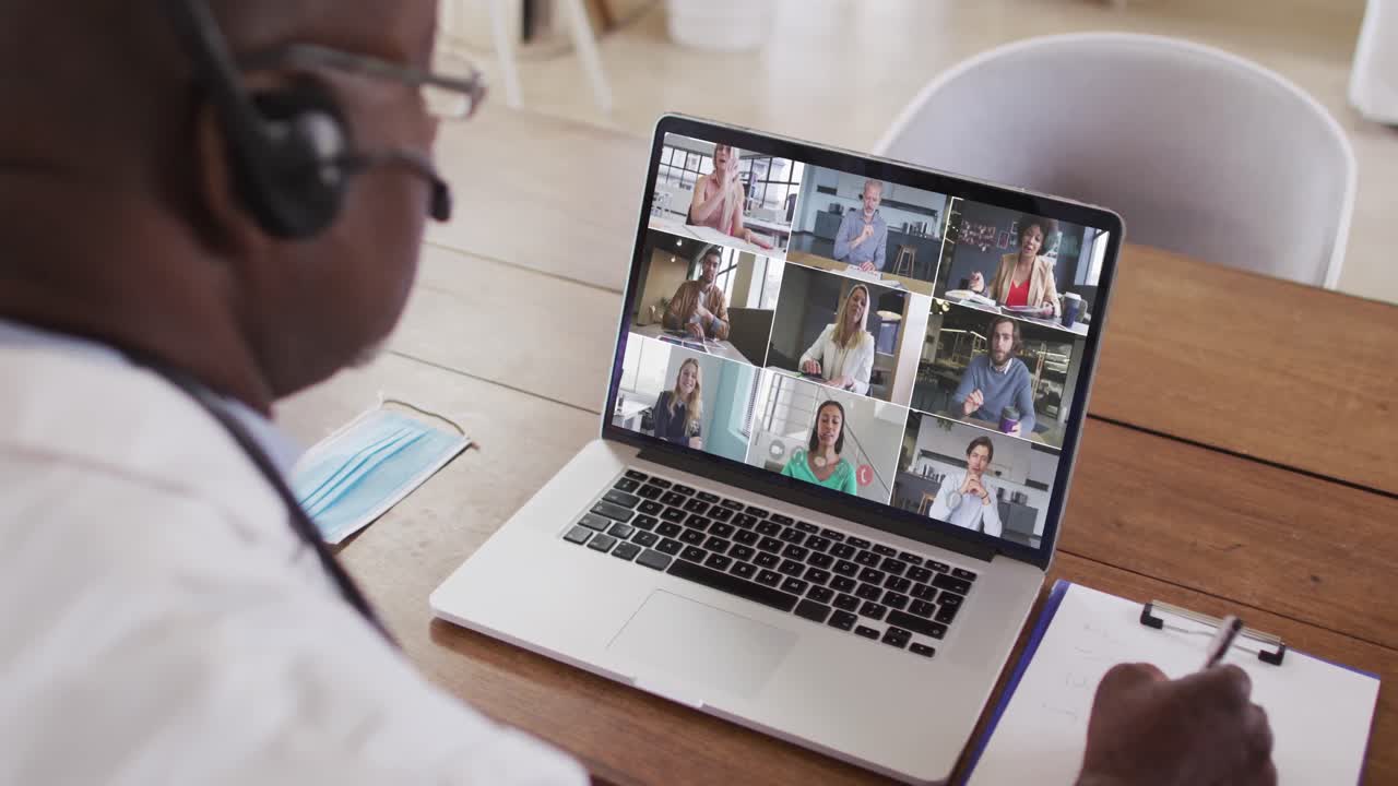 Afroamerikansk mandlig læge, der tager noter under en videokonference på sin bærbare computer