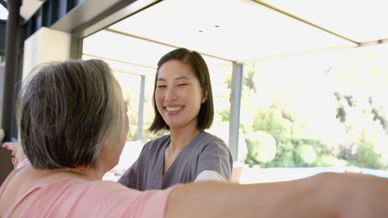 Smiling caregiver assisting senior asian woman with physical therapy exercises at home