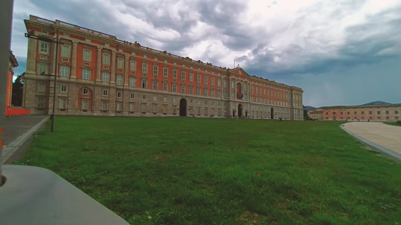 The Royal Palace of Caserta with a vast green lawn under a cloudy sky