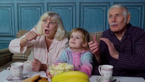 senior grandfather and grandmother happy laughing, eating popcorn, watching cartoons movies at home