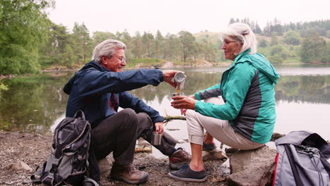 senior couple sitting by a lake drinking coffee during camping holiday, lake district, uk