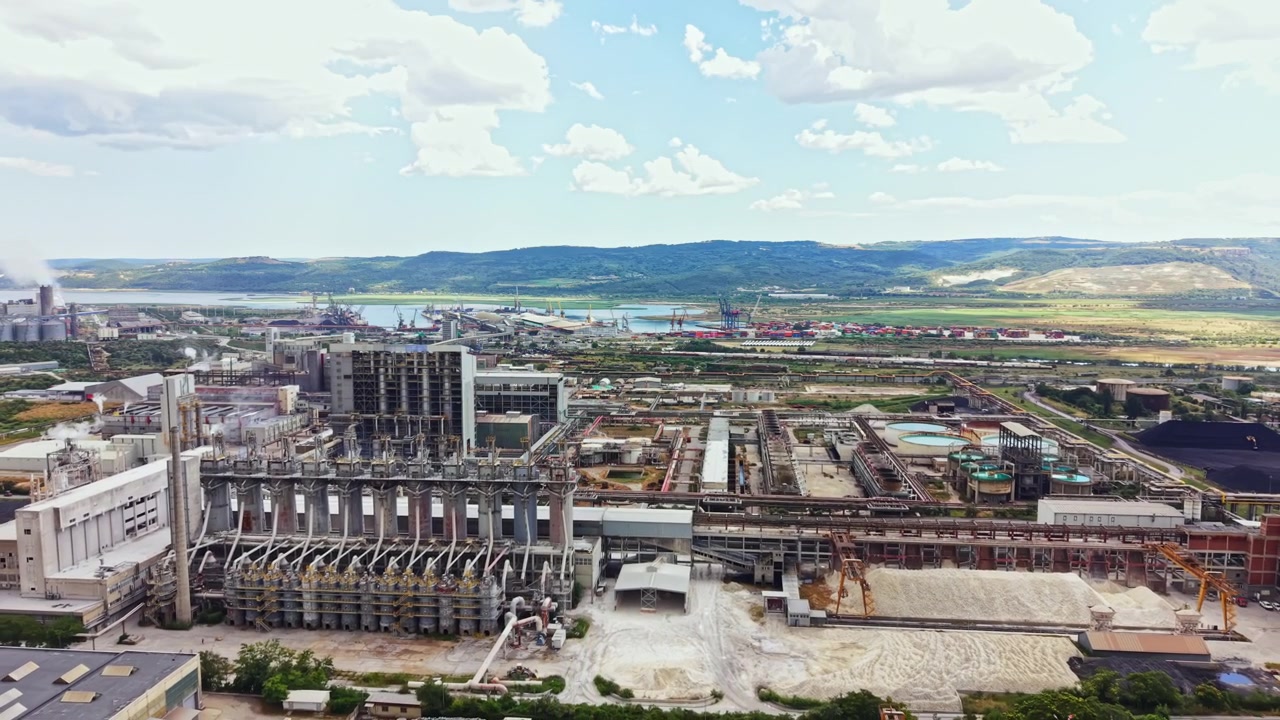 Zona industrial con fábricas, tanques de almacenamiento y muelles de transporte cerca de un río y colinas al fondo durante el día