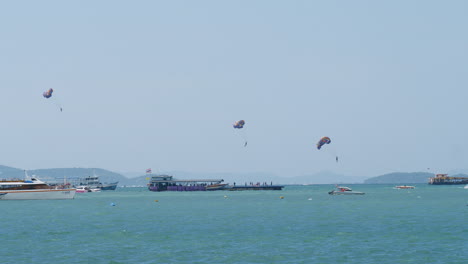 three people parasailing in pattaya as they are being pulled by boat to gain altitude while are other boats are seen, thailand