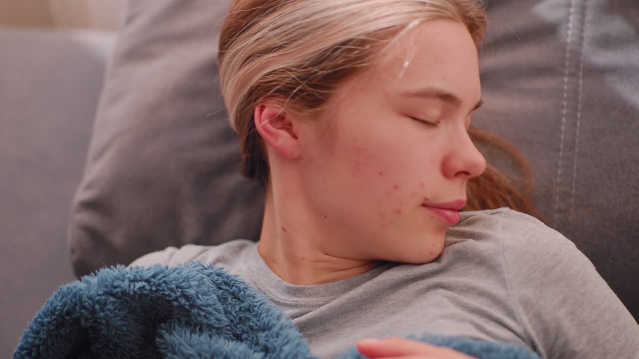 Close up of sleepy girl resting sideways on cushion while adjusting her posture gently with eyes closed under soft sunlight, trying not to wake up during early peaceful indoor moment of rest