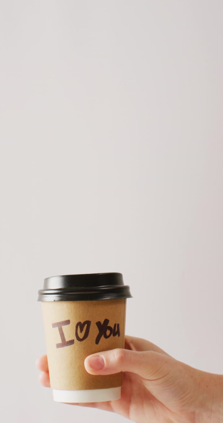 Video verticale di una mano che tiene una tazza di caffè da asporto con la scritta 'I heart you', con spazio per il testo.