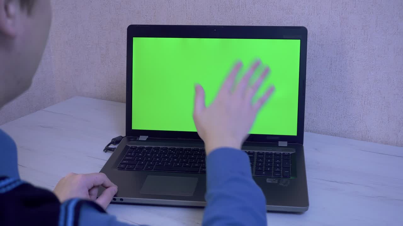 un hombre saluda a sus colegas por video llamada en una computadora portátil y le recuerda que se ponga una máscara protectora, una pantalla de monitor verde