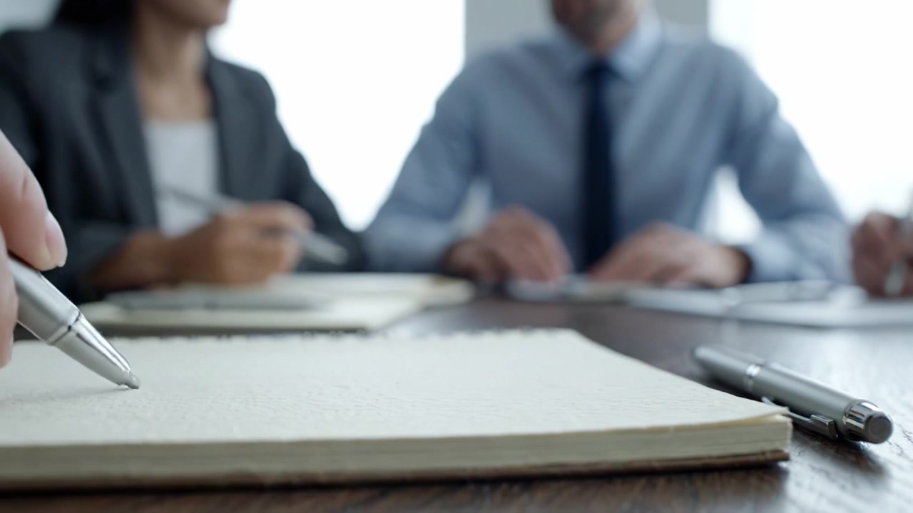 Focus sulle dinamiche della riunione: professionisti impegnati in una discussione con quaderni e penne su un tavolo, che evidenziano la collaborazione e le attività di pianificazione.