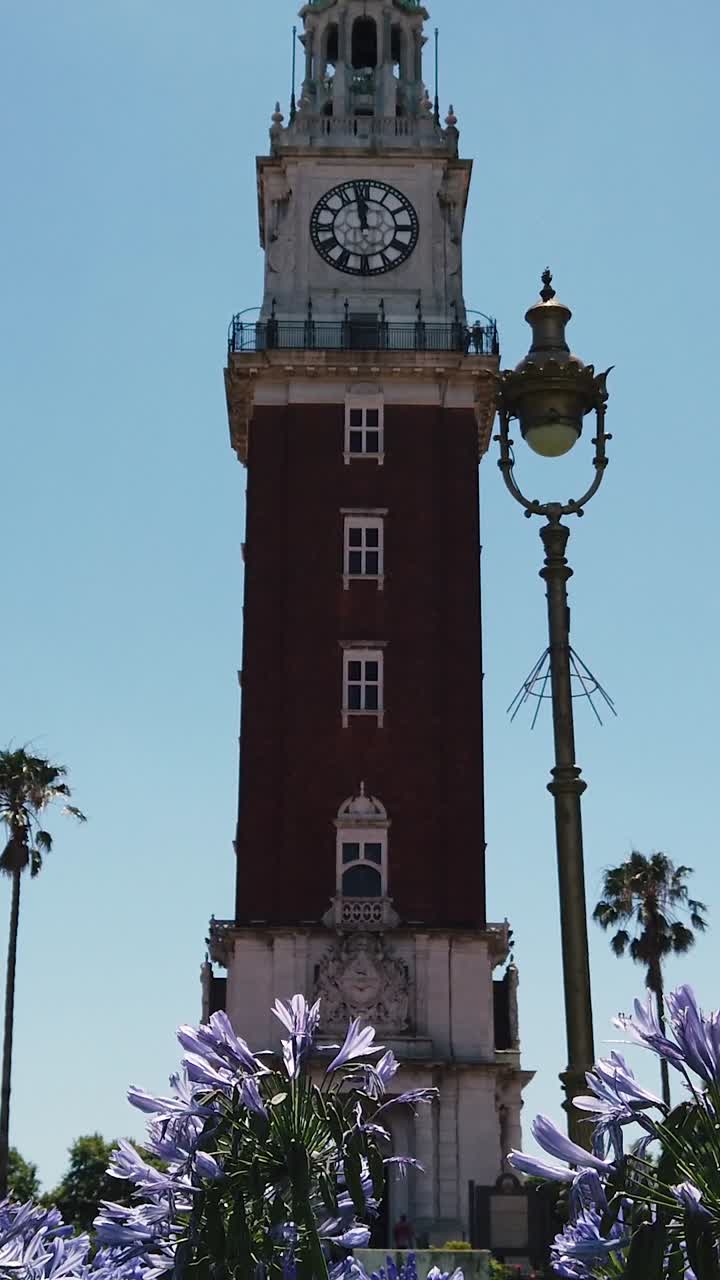 vista vertical monumental torre de la ciudad inglesa reloj sobre flores en buenos aires punto de referencia argentino en retiro, jardín urbano con pájaros volando horizonte