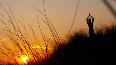 silueta de una mujer de pie en la duna en vrksasana - asana de árbol en los rayos de la puesta de sol