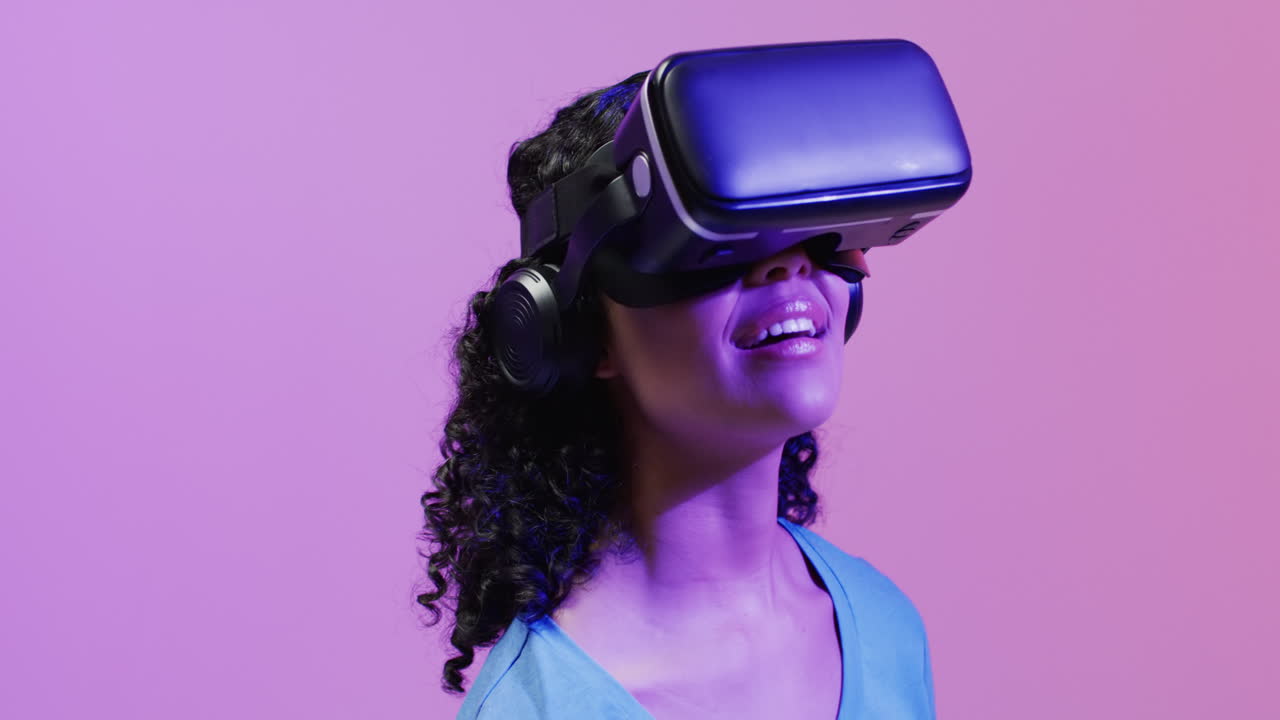 video di una donna biraciale che usa un auricolare vr su sfondo rosa e viola