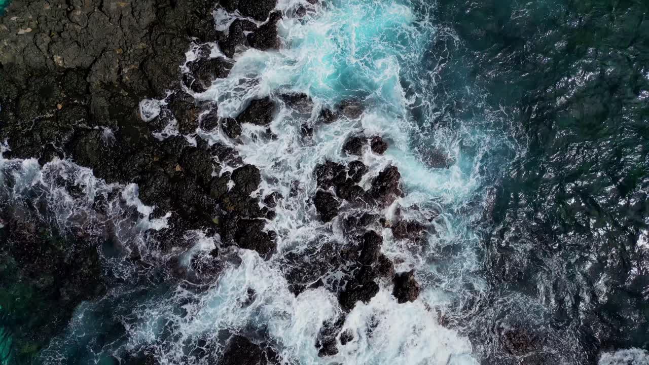 Vista dall'alto, in ascesa, da drone delle onde che si infrangono sulla roccia vulcanica nera