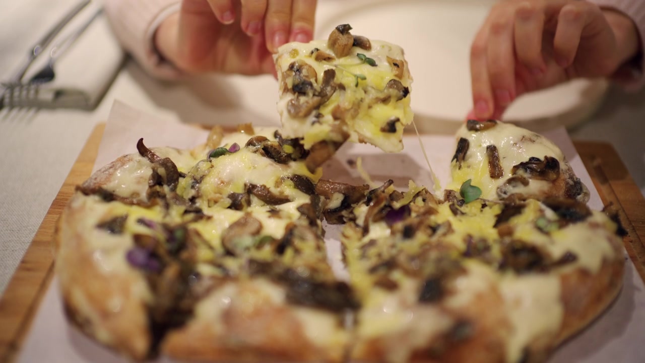 Primo piano di una donna che separa le fette di una pizza ai funghi appena sfornata su un tagliere di legno