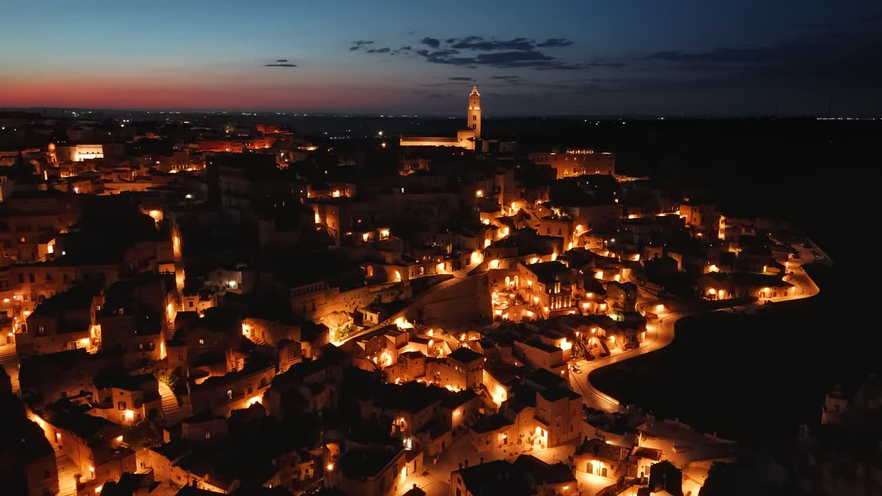 Aerial of Matera Sassi old town illuminated by yellow lights, showing the narrow alleys and churches.