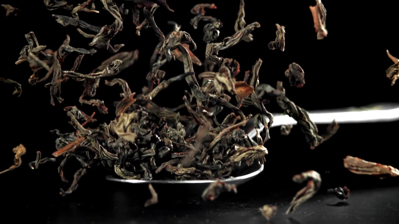 Dry Tea Leaves Falling From Spoon In Slow Motion On Black Background