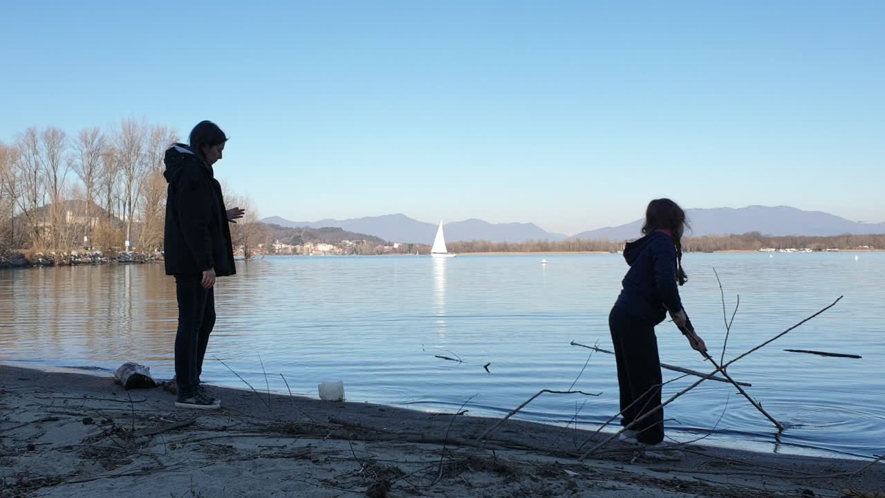 Mother and child playing on lakeside with sailboat in background