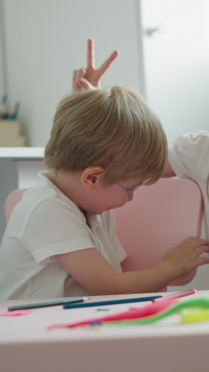 Active siblings dance and clap sitting at desk in playroom at home. Couple of friendly children makes noise playing together. Little boy and girl laugh cheerful