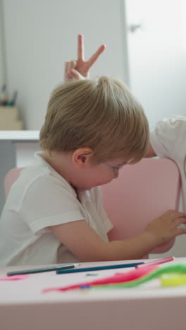 active siblings dance and clap sitting at desk in playroom at home. couple of friendly children makes noise playing together. little boy and girl laugh cheerful