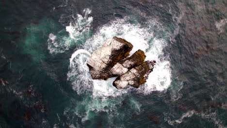 aerial birds eye view of pacific ocean waves crashing against small rock island off big sur