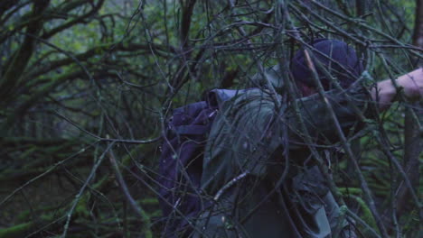 Man-in-wilderness-struggle-through-wooden-branches-during-daytime-on-backpack-trip