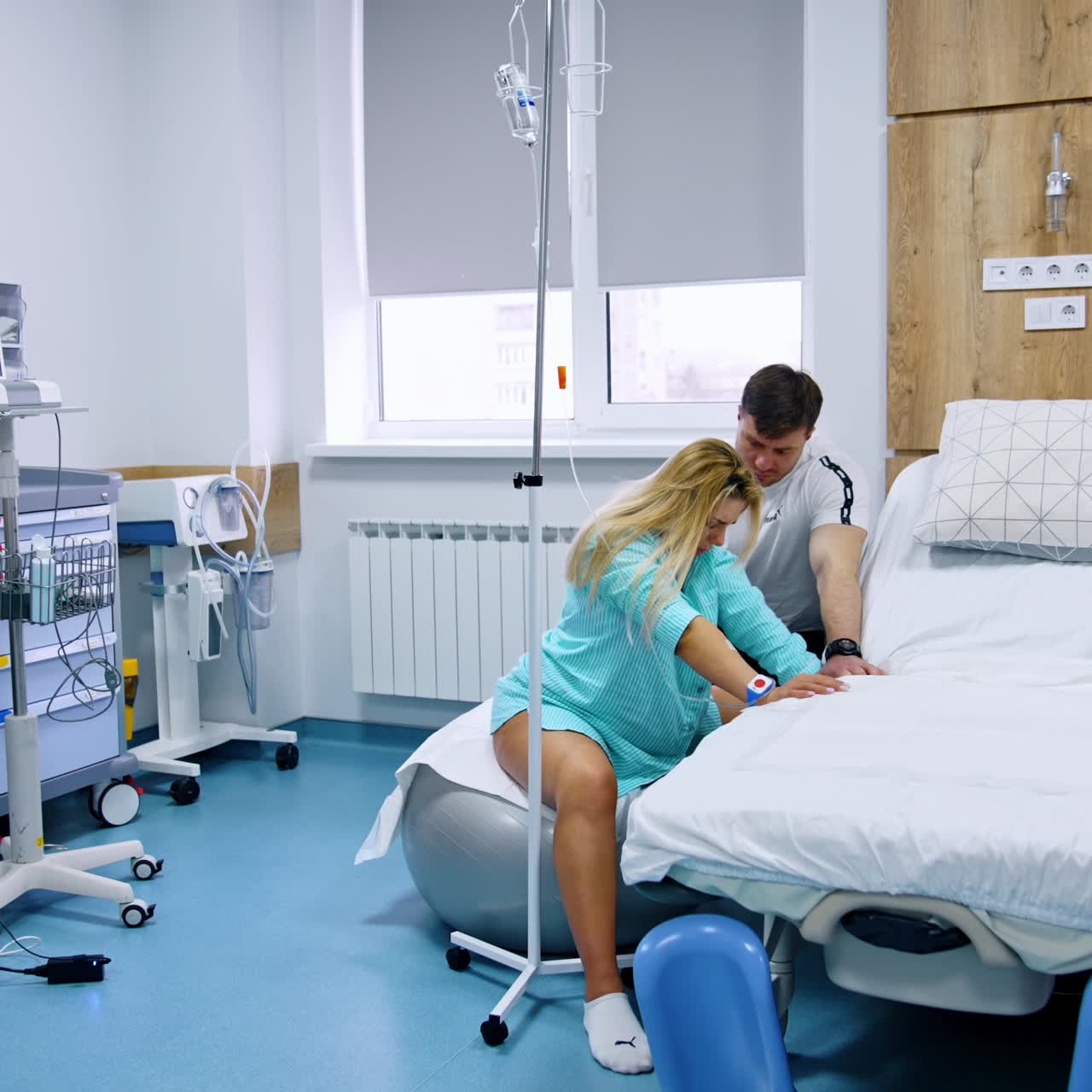 Expecting couple in the hospital ward. Pregnant woman sits on a fitball during contractions. Man soothes his wife