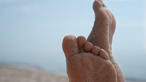 mulher descalça manchada de areia de praia de perto. menina descalça levantando as pernas.