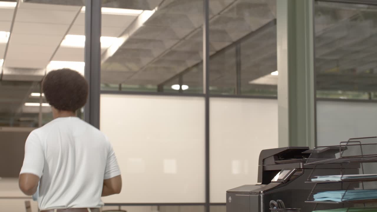 20대 아프리카계 미국인 남성이 사무실 환경에서 20대 다른 두 명의 전문가와 함께 왼쪽에서 오른쪽으로 도리 비디오와 함께 배경에 있습니다.