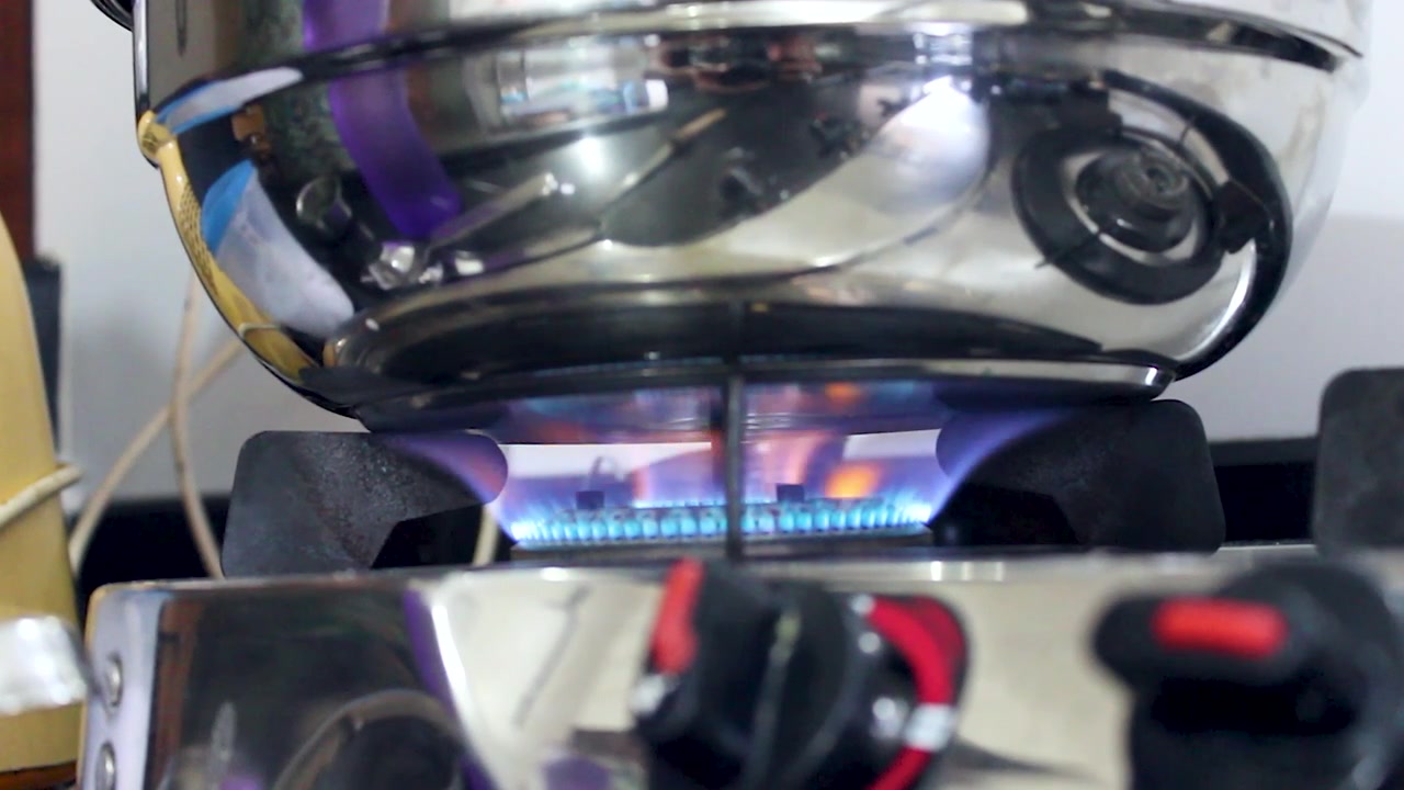 Cinematic close-up of blue gas stove flame heating stainless steel cookware during meal preparation, ideal for cooking, kitchen, energy, and domestic lifestyle projects.