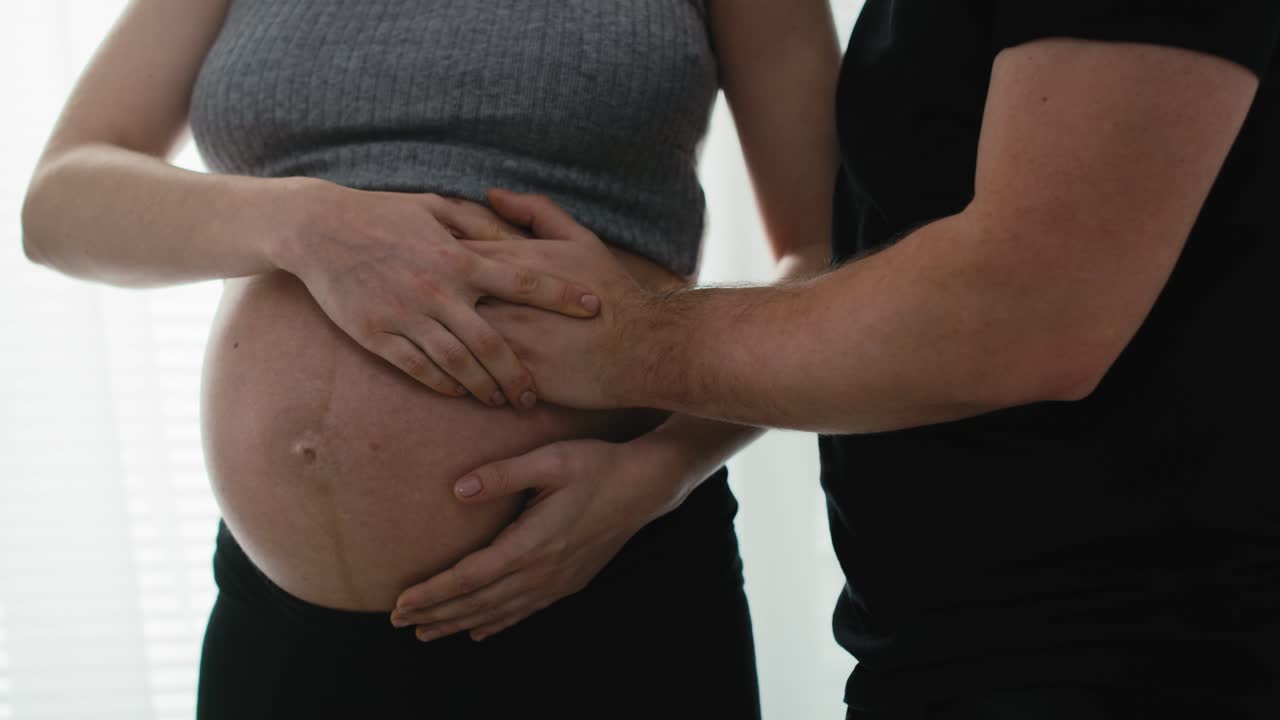 Detail of mother in advanced pregnancy and future father feeling baby's moves.
