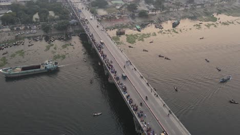 Vista-Giratoria-De-Drones-Sobre-El-Puente-Ocupado-En-El-Río-Buriganga,-Dhaka,-Bangladesh-Y-Vapores-De-Madera-En-La-Orilla-Del-Río