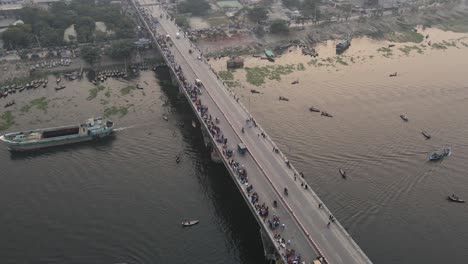 drone rotating view over busy bridge on buriganga river, dhaka, bangladesh, and wooden steamers at riverbank