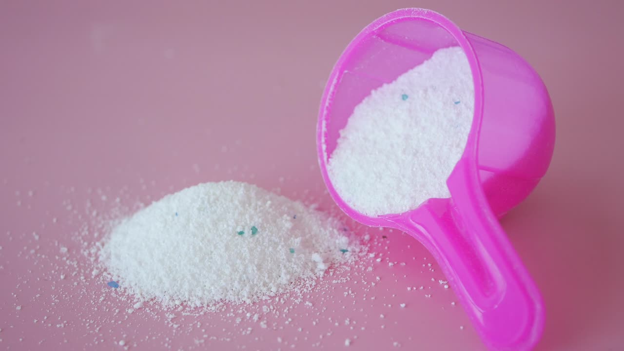 polvo de detergente para la ropa en una cuchara rosada sobre un fondo rosado