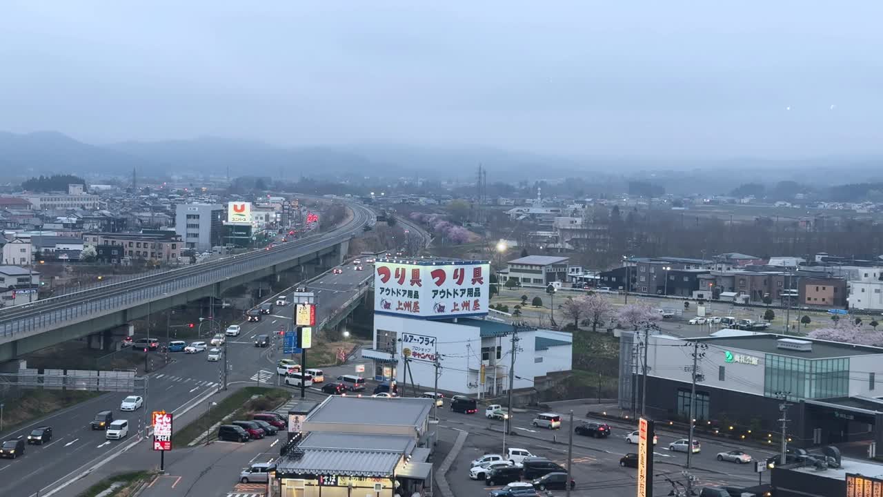 Elevated city view of Aomori Bay with misty skies, roads, traffic, and cherry blossoms