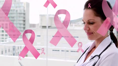 Animation-of-pink-ribbon-cancer-logos-floating-over-smiling-female-doctor-using-tablet