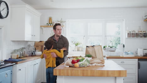 Padre-E-Hijo-Regresan-A-Casa-Después-De-Un-Viaje-De-Compras-Usando-Bolsas-Sin-Plástico-Desempacando-Alimentos-En-La-Cocina