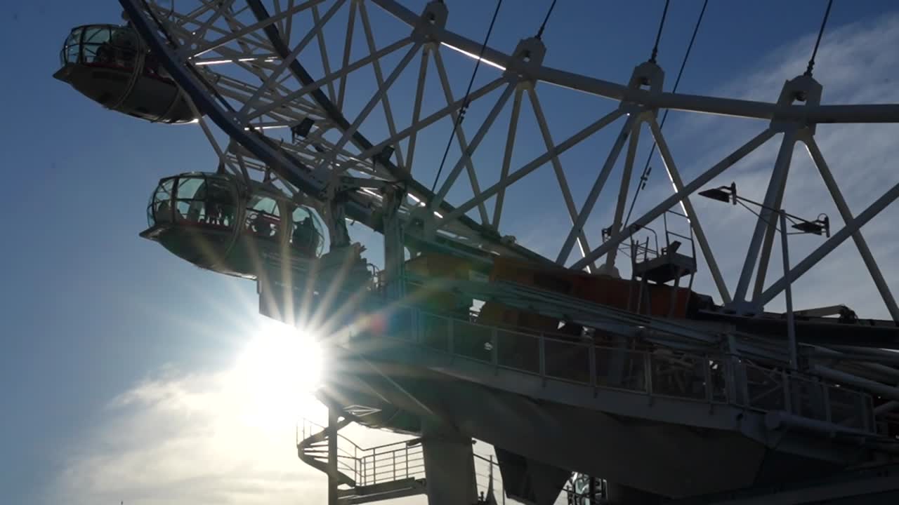London Eye ferris wheel with sunbeams shining through as capsules move against blue sky