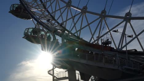 london eye ferris wheel with sunbeams shining through as capsules move against blue sky