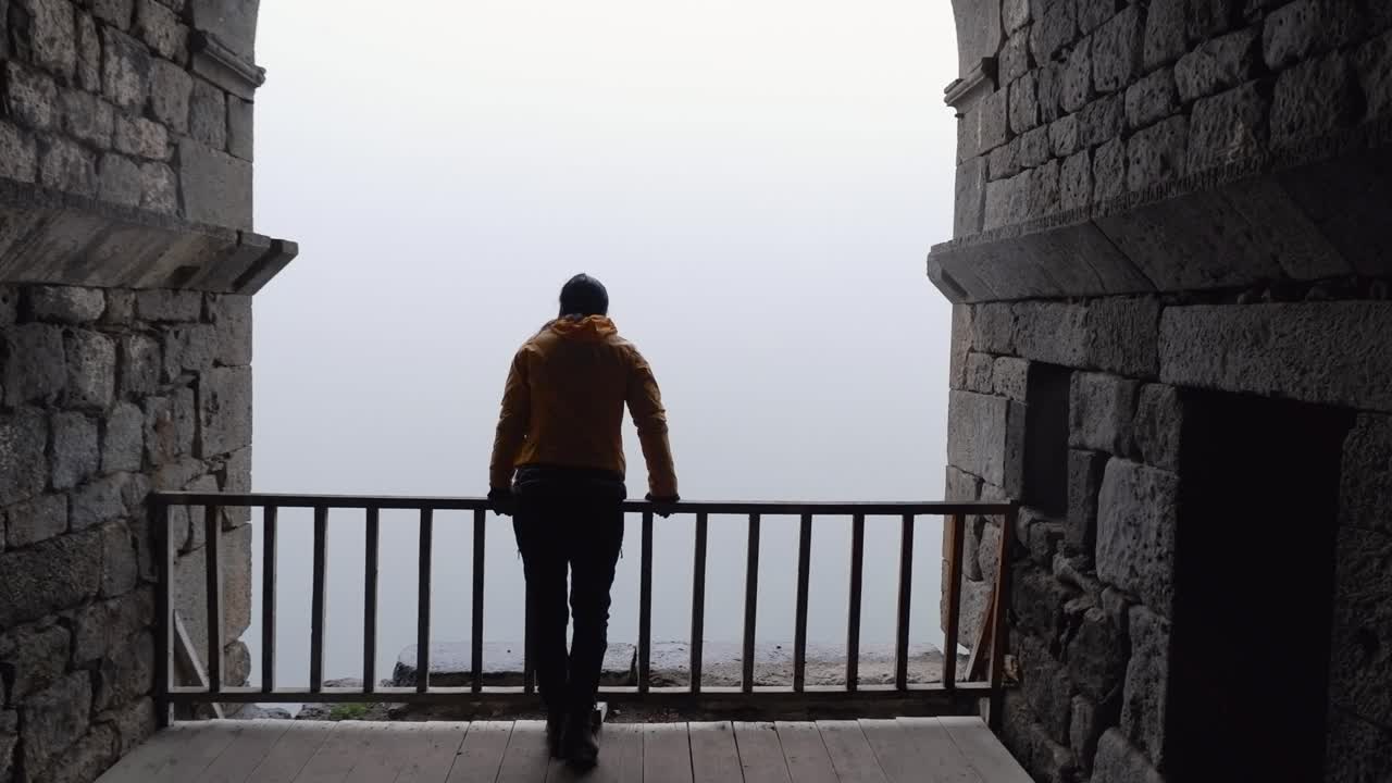 Donna cammina verso la balaustra in una vecchia chiesa, guardando fuori verso una giornata nebbiosa