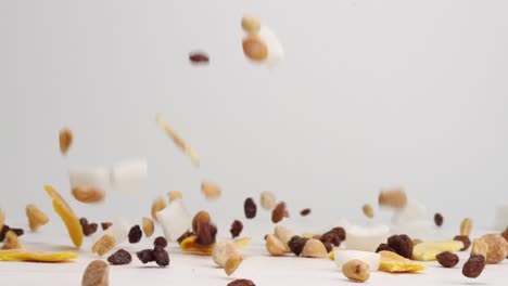 sweet and salty tropical trail mix with dried fruit slices, coconut, raisins and nuts falling onto white table top and bouncing into a pile in slow motion