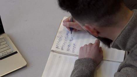 musician wearing brown long sleeves writing music notes on blank music sheet  - close up shot