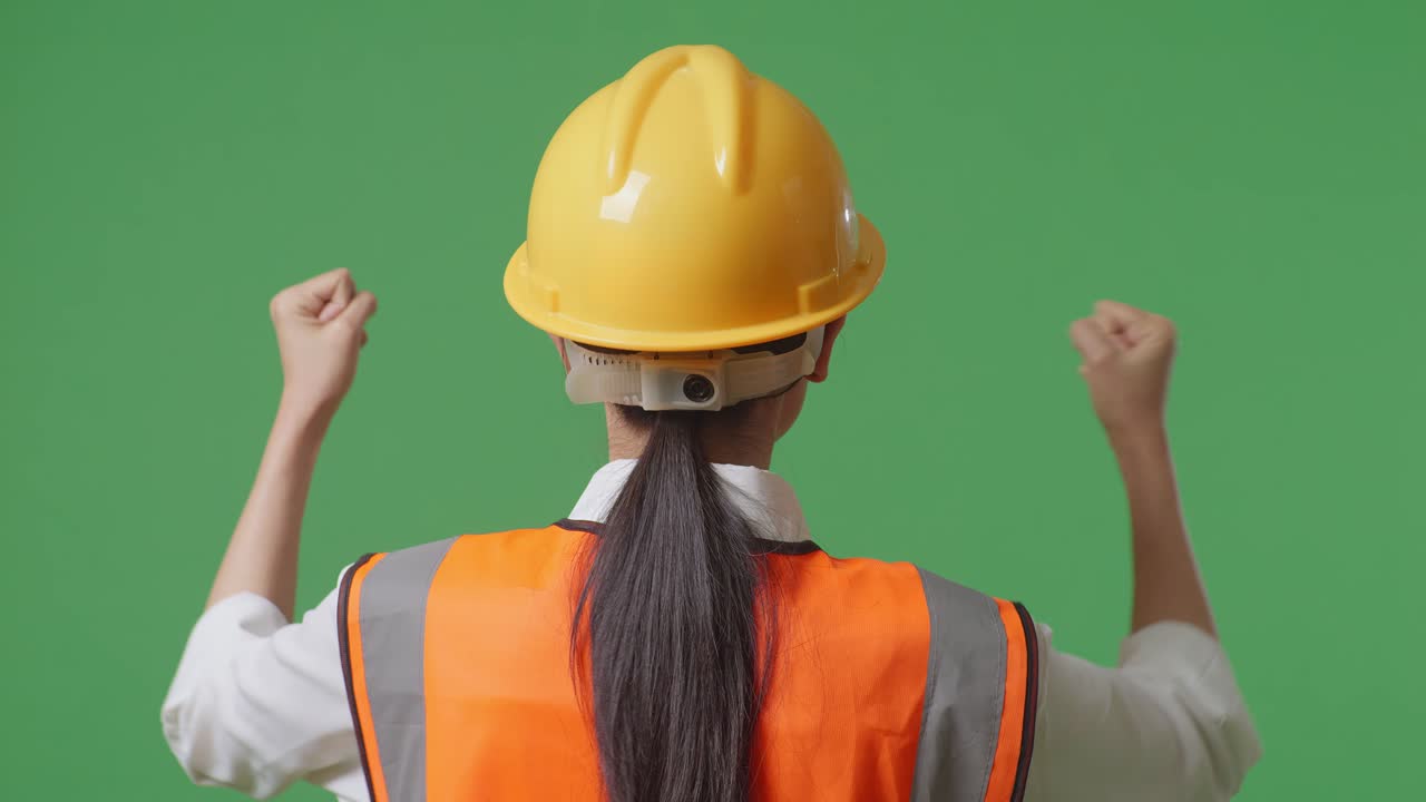 vista posterior cercana de una ingeniera con casco de seguridad levantando las manos celebrando mientras trabaja en el estudio de fondo de la pantalla verde