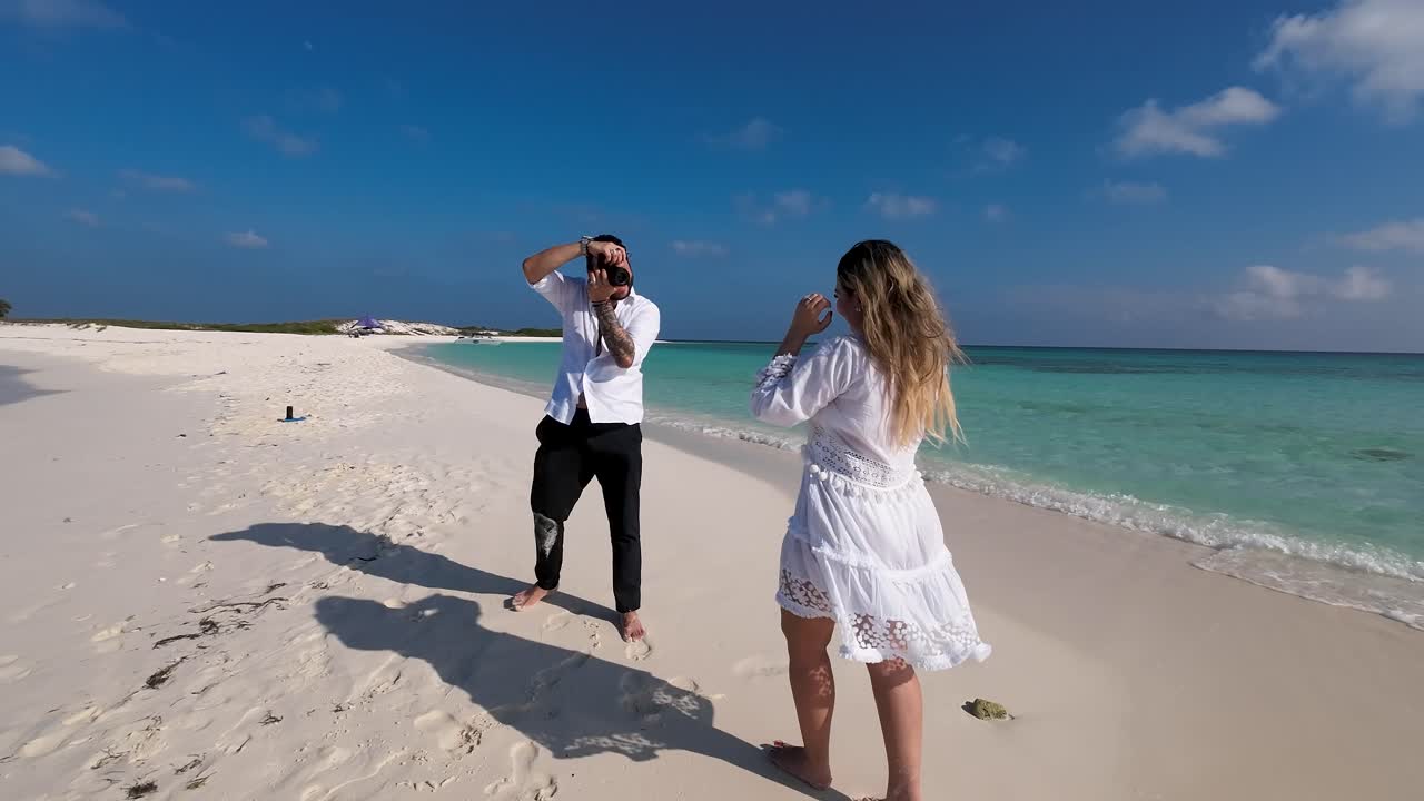 Fotograaf die foto's maakt van een vrouwelijk model in het wit op het strand bij zonsondergang.