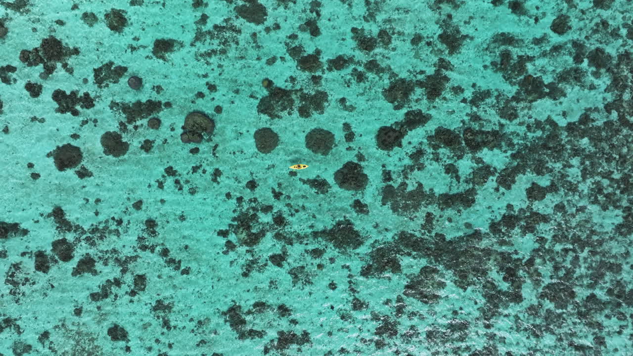 High angle drone descends top down on solo kayaker in middle of clear ocean water