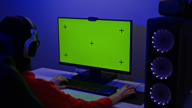 Gamer sits at a large computer monitor with a green screen. Powerful personal computer for computer game lovers, a dark room with illumination. Back view. 4k, ProRes
